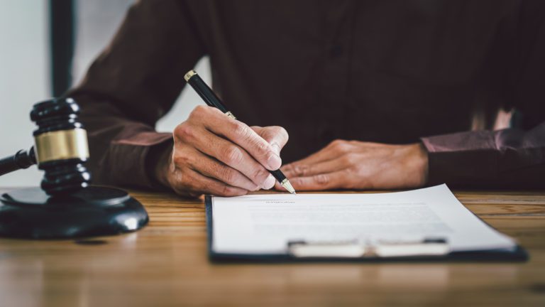 Close up lawyer hands holding pen to sign a contract, sitting at desk.